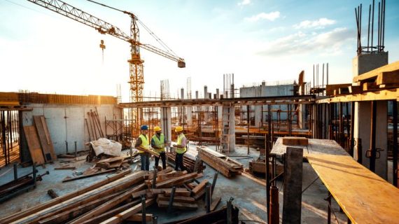 Construction industry concept - architects and engineers discussing work progress between concrete walls, scaffolds and cranes.